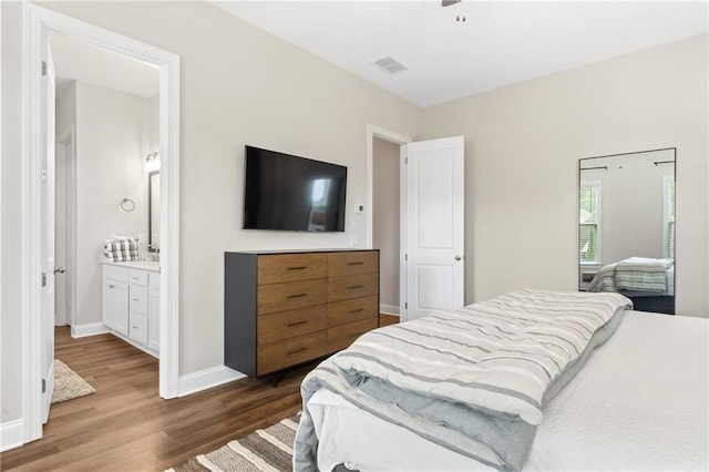 bedroom with connected bathroom, a ceiling fan, baseboards, wood finished floors, and visible vents