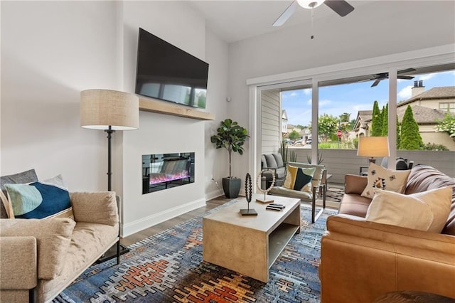 living room featuring baseboards, a ceiling fan, a glass covered fireplace, and wood finished floors