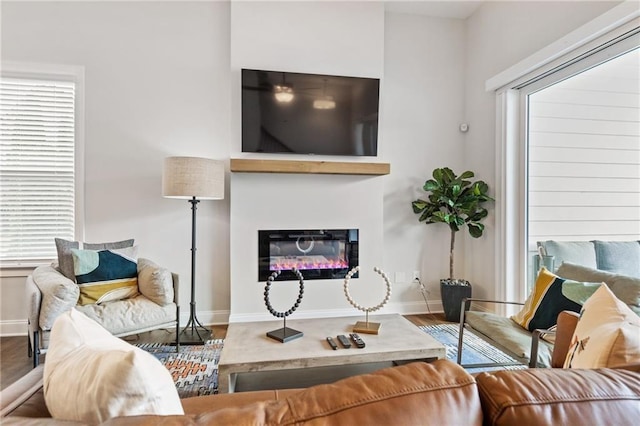 living room featuring a glass covered fireplace, baseboards, and wood finished floors