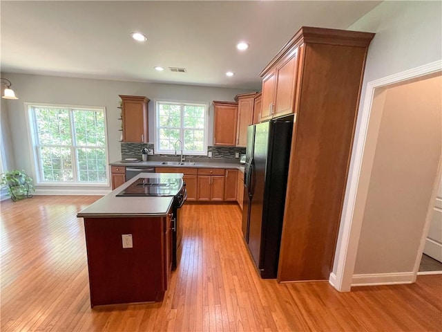 kitchen with decorative backsplash, black fridge, sink, a center island, and plenty of natural light