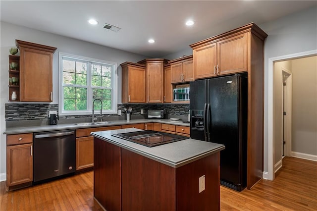 kitchen with tasteful backsplash, sink, black appliances, light hardwood / wood-style flooring, and a center island