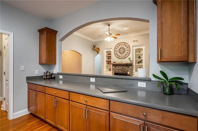 kitchen featuring hardwood / wood-style floors, built in shelves, ceiling fan, ornamental molding, and a fireplace