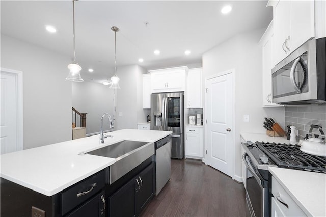 kitchen featuring sink, hanging light fixtures, stainless steel appliances, an island with sink, and decorative backsplash