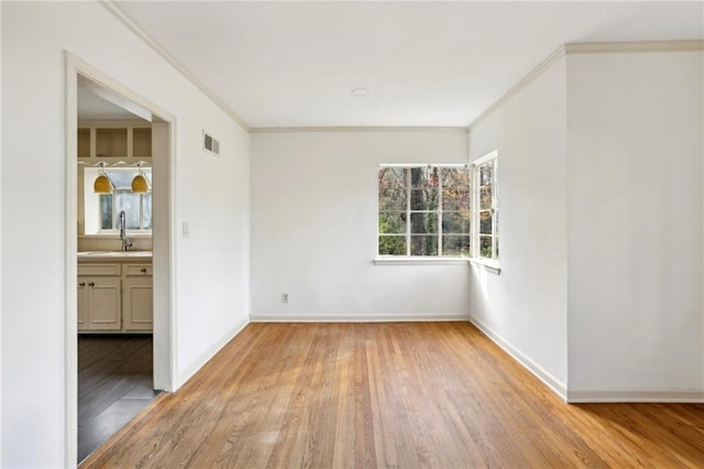 unfurnished room featuring sink, light hardwood / wood-style floors, and ornamental molding