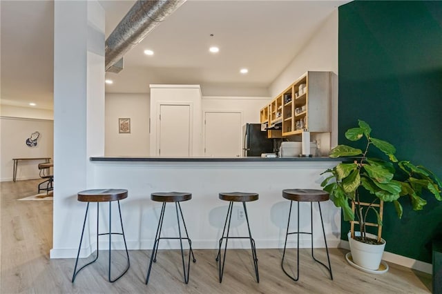 kitchen featuring freestanding refrigerator, a breakfast bar area, wood finished floors, and recessed lighting