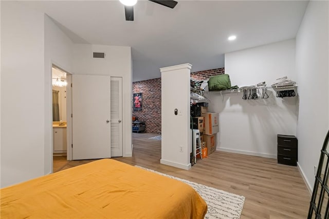 bedroom with brick wall, light wood finished floors, ensuite bathroom, and visible vents