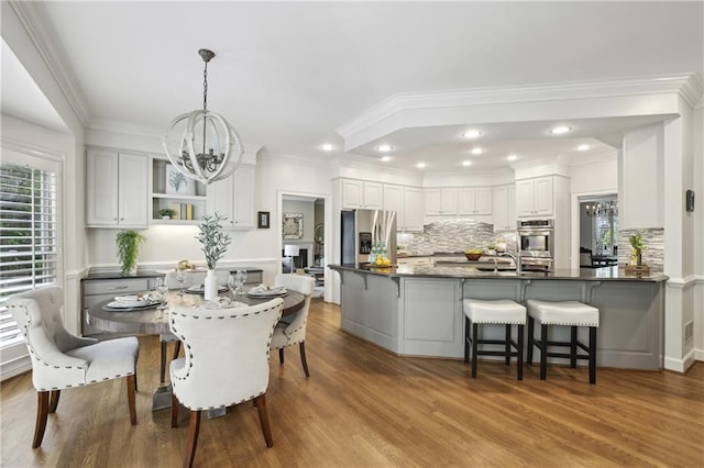 dining area with a chandelier, wood finished floors, ornamental molding, and recessed lighting