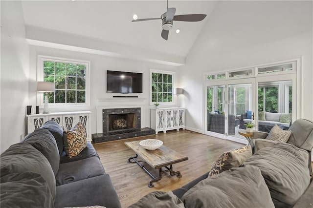 living area with high vaulted ceiling, ceiling fan, plenty of natural light, a fireplace, and wood finished floors