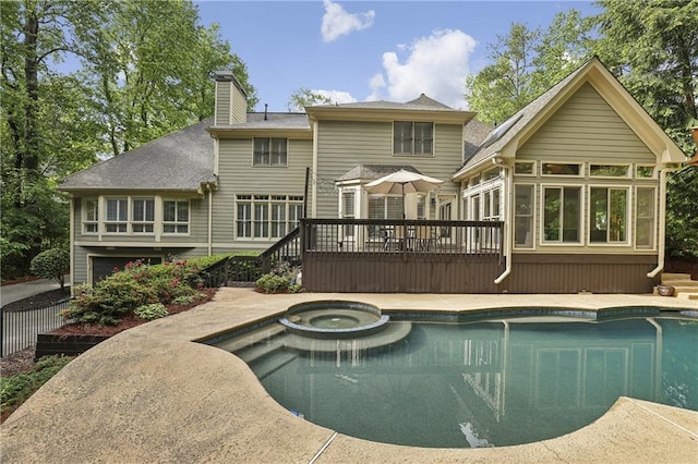 rear view of property featuring a wooden deck, a chimney, a pool with connected hot tub, and roof with shingles