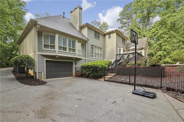 back of house with asphalt driveway, fence, an attached garage, central air condition unit, and a chimney
