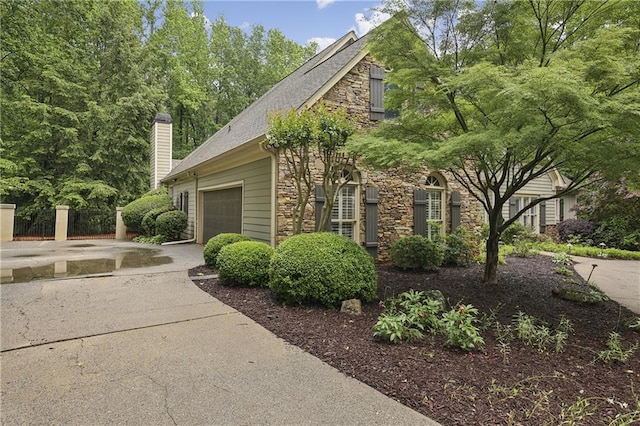 view of home's exterior with stone siding, a garage, a chimney, concrete driveway, and a shingled roof