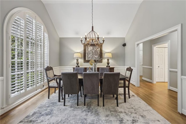 dining area with a chandelier, light wood-style floors, wainscoting, and high vaulted ceiling