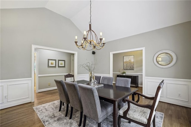 dining area with a chandelier, a wainscoted wall, wood finished floors, a decorative wall, and high vaulted ceiling