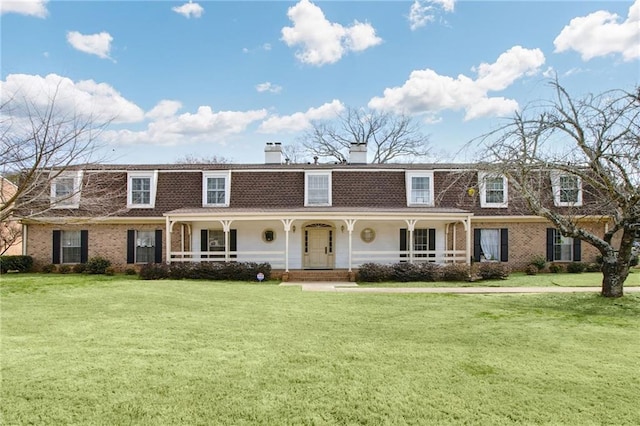 view of front facade featuring covered porch, brick siding, a chimney, and a front yard