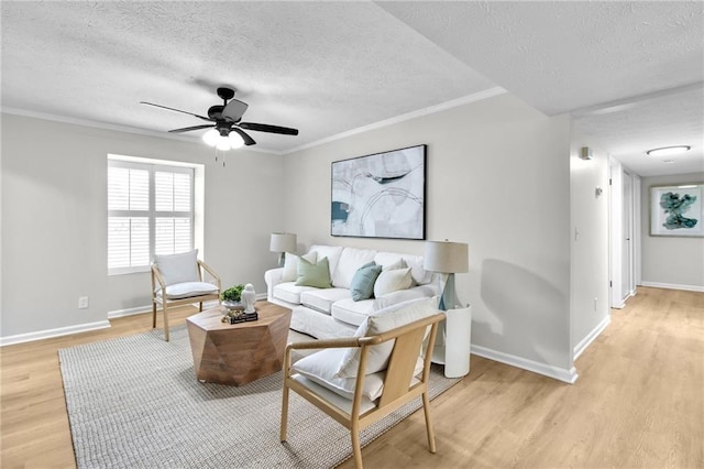 living area featuring a textured ceiling, light wood finished floors, ornamental molding, and baseboards