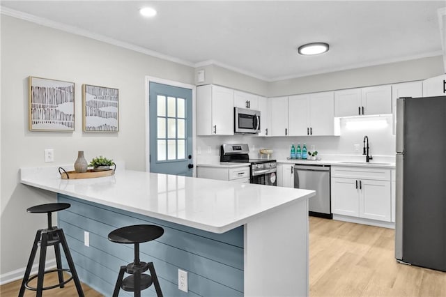 kitchen featuring appliances with stainless steel finishes, a kitchen breakfast bar, a peninsula, crown molding, and a sink