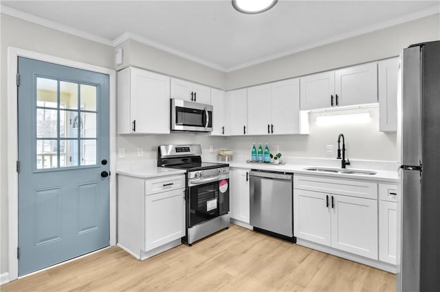 kitchen with light wood finished floors, ornamental molding, stainless steel appliances, light countertops, and a sink