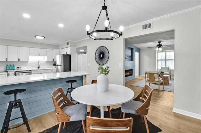 dining room featuring a large fireplace, light wood finished floors, visible vents, and crown molding