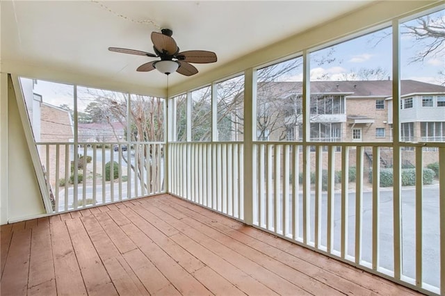 unfurnished sunroom with a healthy amount of sunlight, a residential view, and a ceiling fan