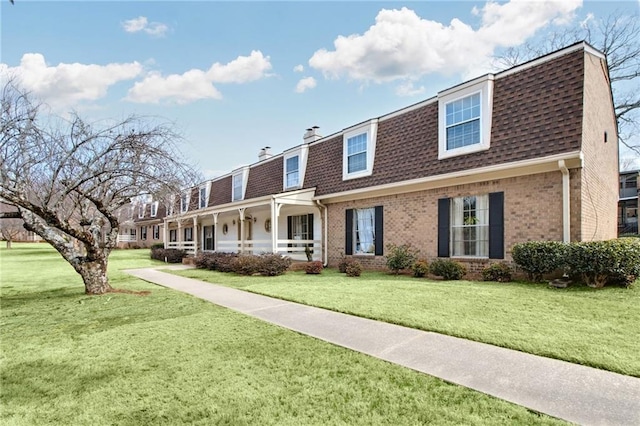 view of front of house featuring roof with shingles, brick siding, a chimney, and a front lawn