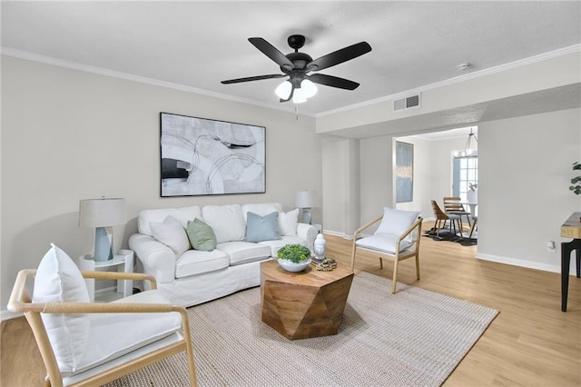 living room with crown molding, visible vents, light wood-style flooring, baseboards, and ceiling fan with notable chandelier