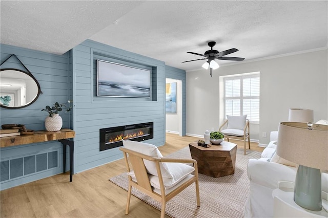 living area with ceiling fan, a textured ceiling, light wood-style flooring, a fireplace, and visible vents