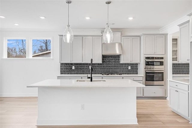 kitchen featuring gray cabinets, decorative light fixtures, ventilation hood, a kitchen island with sink, and stainless steel appliances