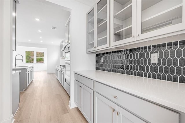 kitchen with oven, sink, decorative backsplash, and light wood-type flooring