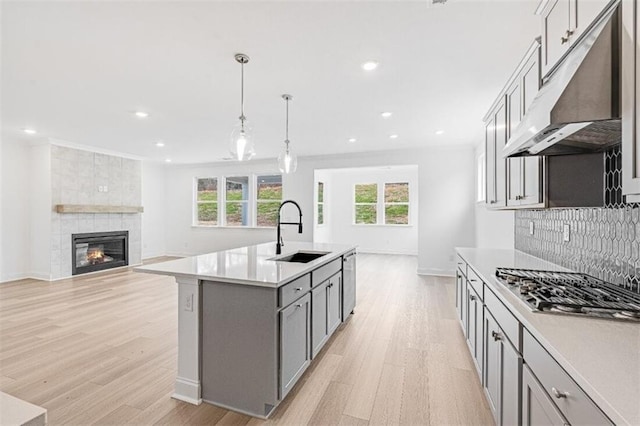 kitchen with sink, gray cabinetry, hanging light fixtures, stainless steel appliances, and a kitchen island with sink