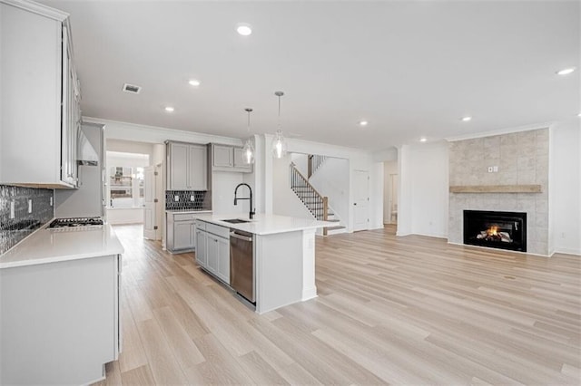 kitchen with a center island with sink, gray cabinets, pendant lighting, stainless steel appliances, and a fireplace