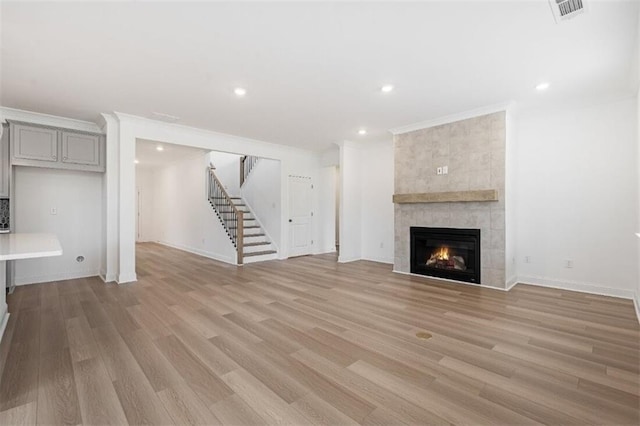 unfurnished living room with crown molding, a tiled fireplace, and light hardwood / wood-style flooring