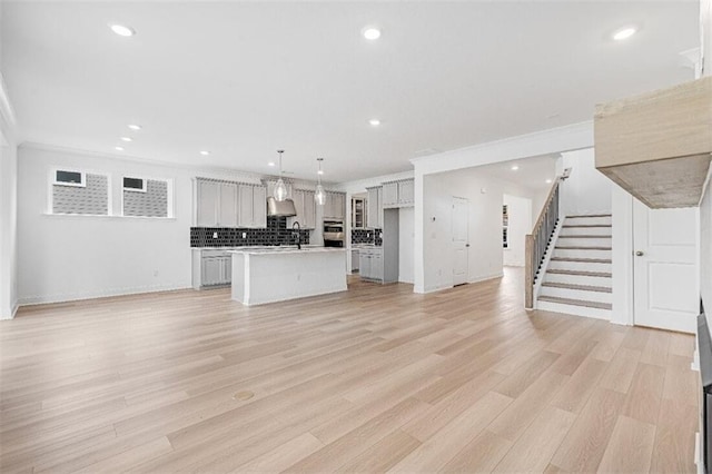 unfurnished living room featuring ornamental molding, sink, and light hardwood / wood-style floors