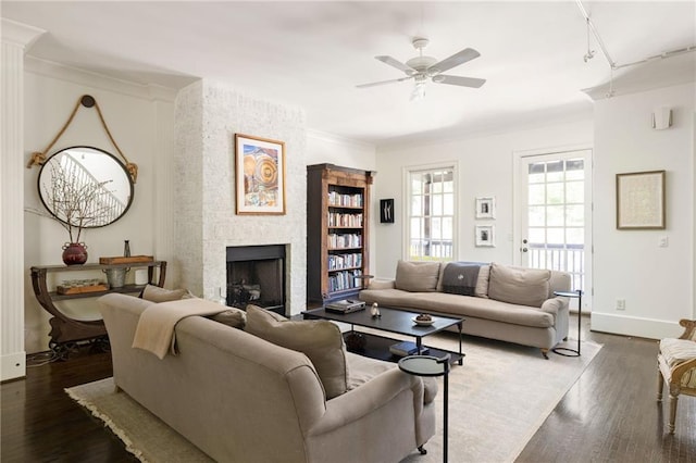 living room with ornamental molding, baseboards, dark wood finished floors, a large fireplace, and a ceiling fan