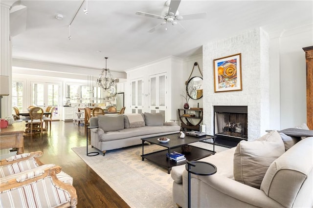 living area featuring ceiling fan with notable chandelier, a fireplace, wood finished floors, and ornamental molding
