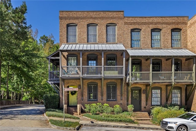 view of property with a balcony, metal roof, a standing seam roof, and brick siding