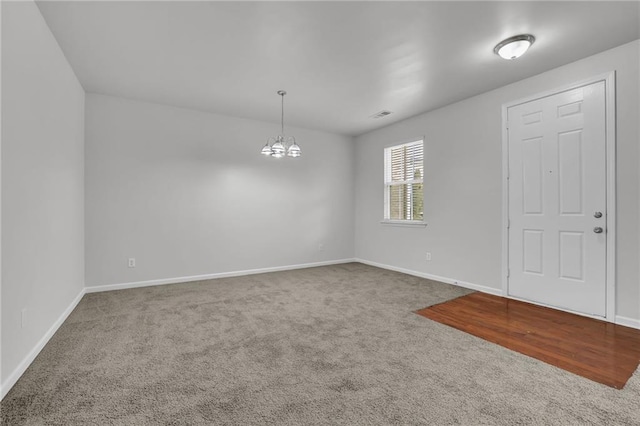 unfurnished room featuring baseboards, visible vents, an inviting chandelier, and carpet floors