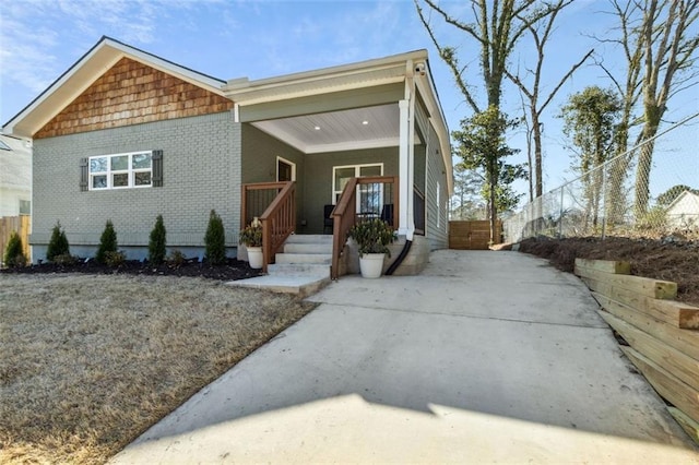 view of front of home with covered porch, brick siding, and fence