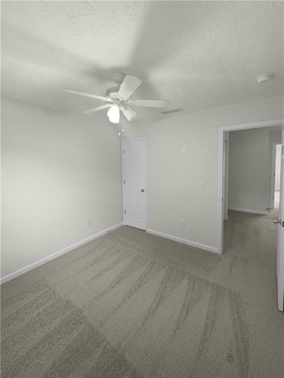 carpeted empty room with ceiling fan and a textured ceiling