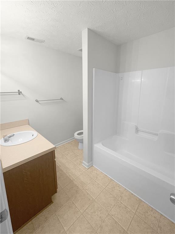 full bathroom with tub / shower combination, vanity, a textured ceiling, toilet, and tile patterned floors