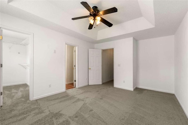 unfurnished bedroom featuring a spacious closet, a tray ceiling, ceiling fan, and carpet floors