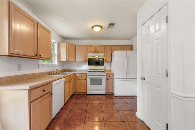 kitchen with light brown cabinets, dark tile patterned flooring, sink, white appliances, and a textured ceiling