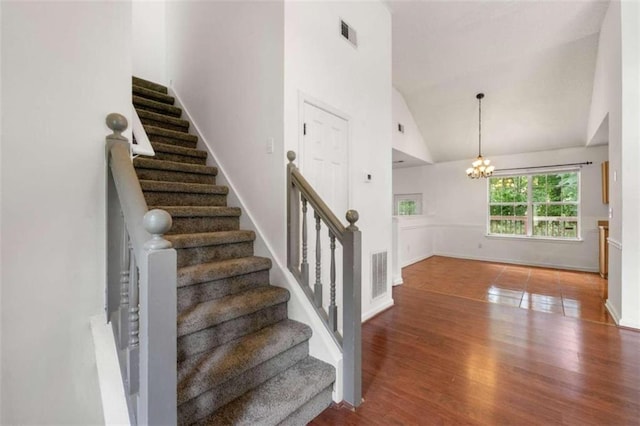 stairs featuring a chandelier, hardwood / wood-style floors, and high vaulted ceiling