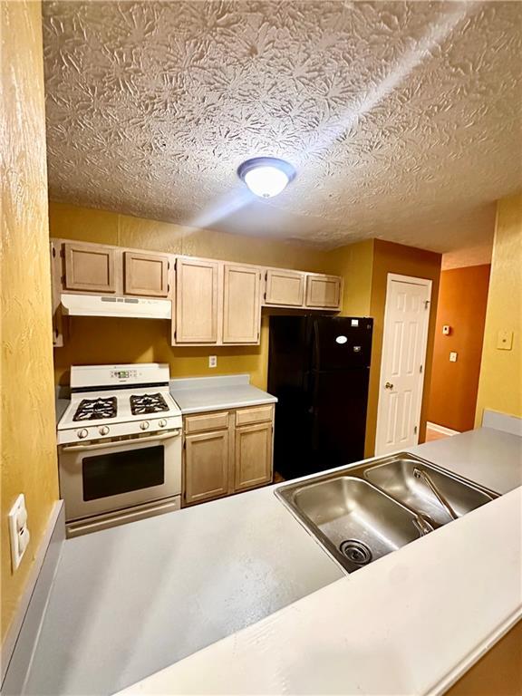 3793 Mays Ct SW, Atlanta, GA 30331 - kitchen featuring white range with gas stovetop, freestanding refrigerator, under cabinet range hood, light countertops, and a sink