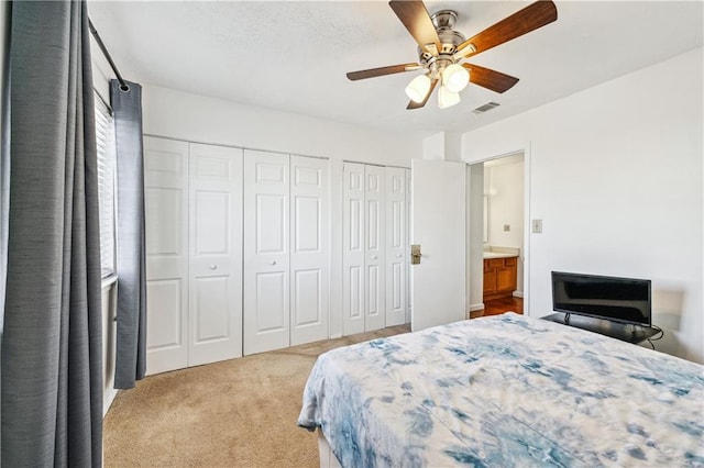 carpeted bedroom featuring multiple closets, visible vents, and ceiling fan