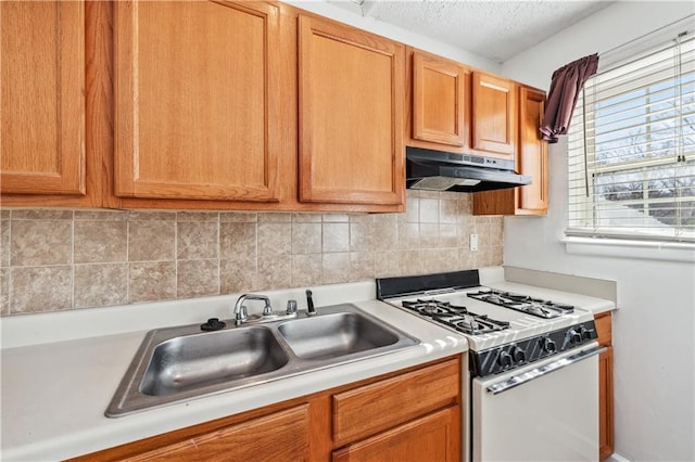 kitchen featuring light countertops, gas range gas stove, a sink, and under cabinet range hood