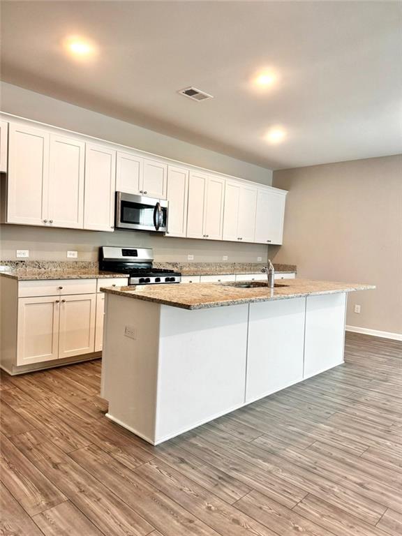 kitchen with stainless steel appliances, an island with sink, and light hardwood / wood-style flooring