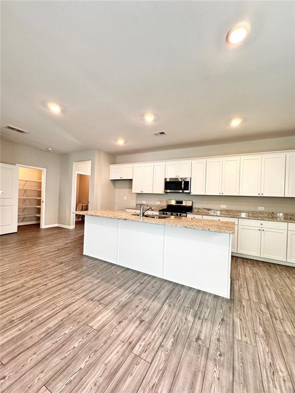 kitchen featuring white cabinets, appliances with stainless steel finishes, light stone countertops, light hardwood / wood-style floors, and an island with sink