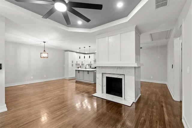 unfurnished living room featuring a tray ceiling, ceiling fan, sink, wood-type flooring, and a premium fireplace