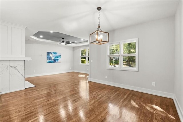 unfurnished dining area featuring hardwood / wood-style flooring, ceiling fan with notable chandelier, and a tray ceiling