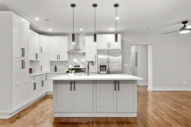 kitchen with white cabinetry, wall chimney range hood, an island with sink, and appliances with stainless steel finishes